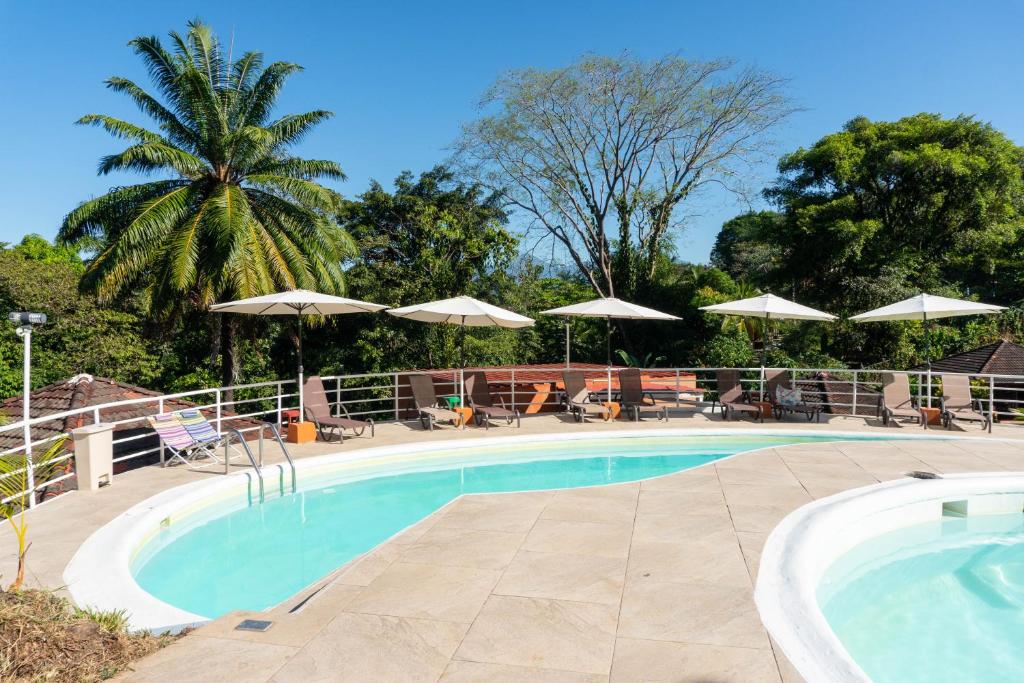una piscina con mesas, sillas y sombrillas en Bongo - Adults Only, en Manuel Antonio
