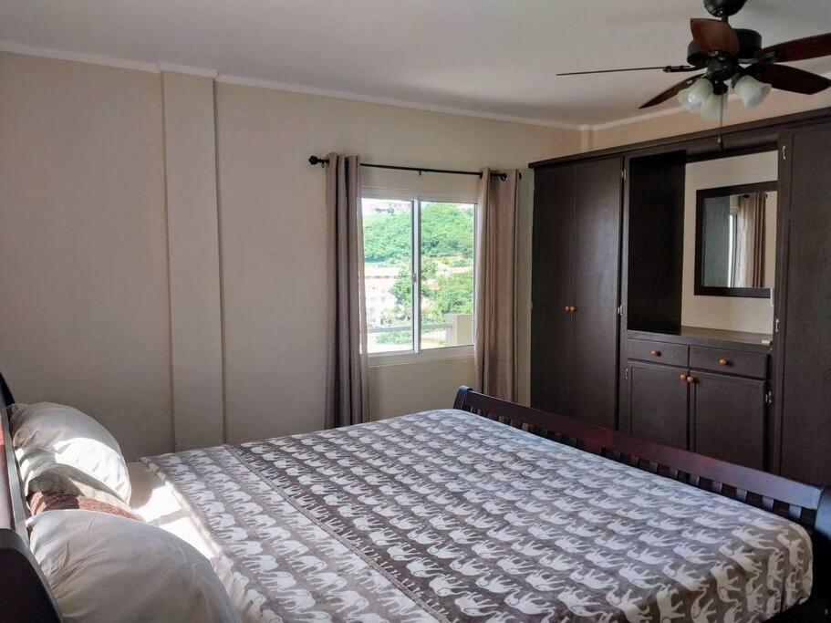 um quarto com uma cama, uma ventoinha de tecto e uma janela em 2BR apt near restaurant, beach, nightlife & convenience store em Lance aux Épines