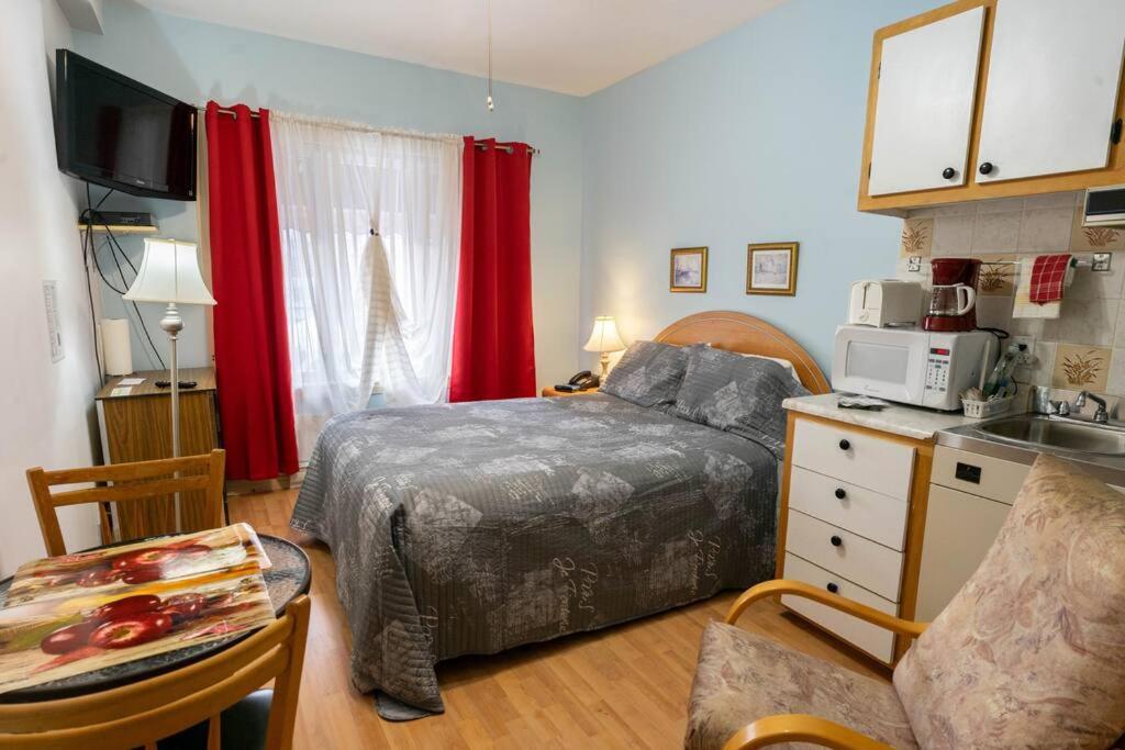 a bedroom with a bed and a kitchen with red curtains at 235 Véranda sous tout son charme in Trois-Rivières
