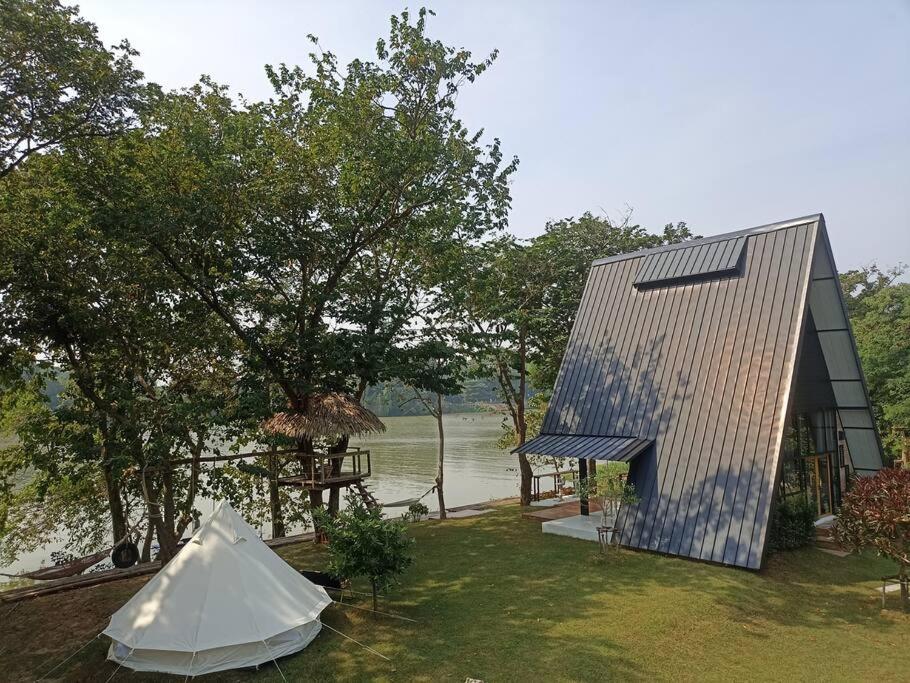 una casa con techo y una tienda en el césped en Kaitoon's River House en Ratchaburi