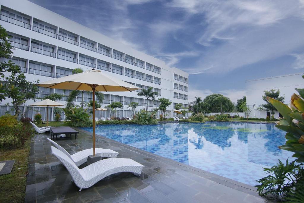 a hotel with a large swimming pool with chairs and an umbrella at Raja Hotel Kuta Mandalika Resort & Convention in Kuta Lombok