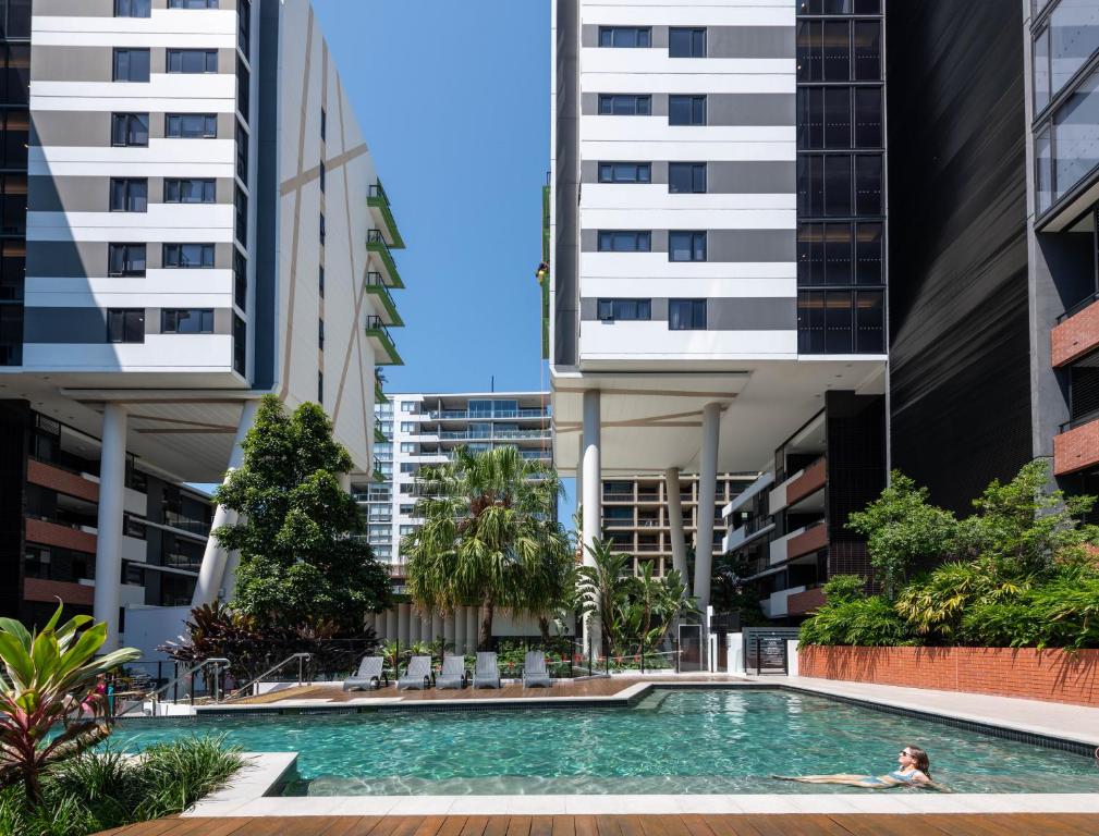 a person swimming in a pool in the middle of buildings at Arena Apartments by CLLIX in Brisbane