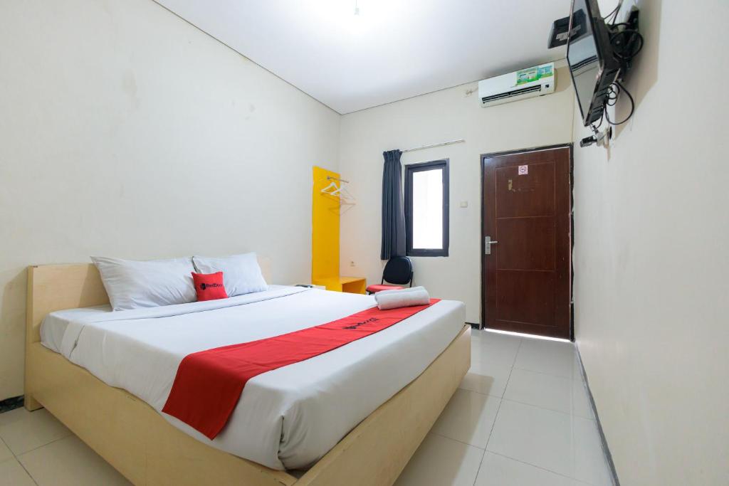 een slaapkamer met een groot bed en een rode deken bij RedDoorz at Osuko Residence Sukomanunggal Jaya in Surabaya