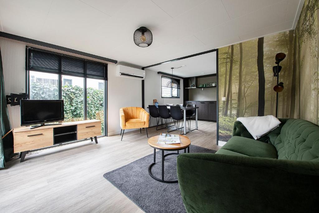 uma sala de estar com um sofá verde e uma televisão em 20, Nestled in the woods, Big Chalet and Garden! em Oisterwijk