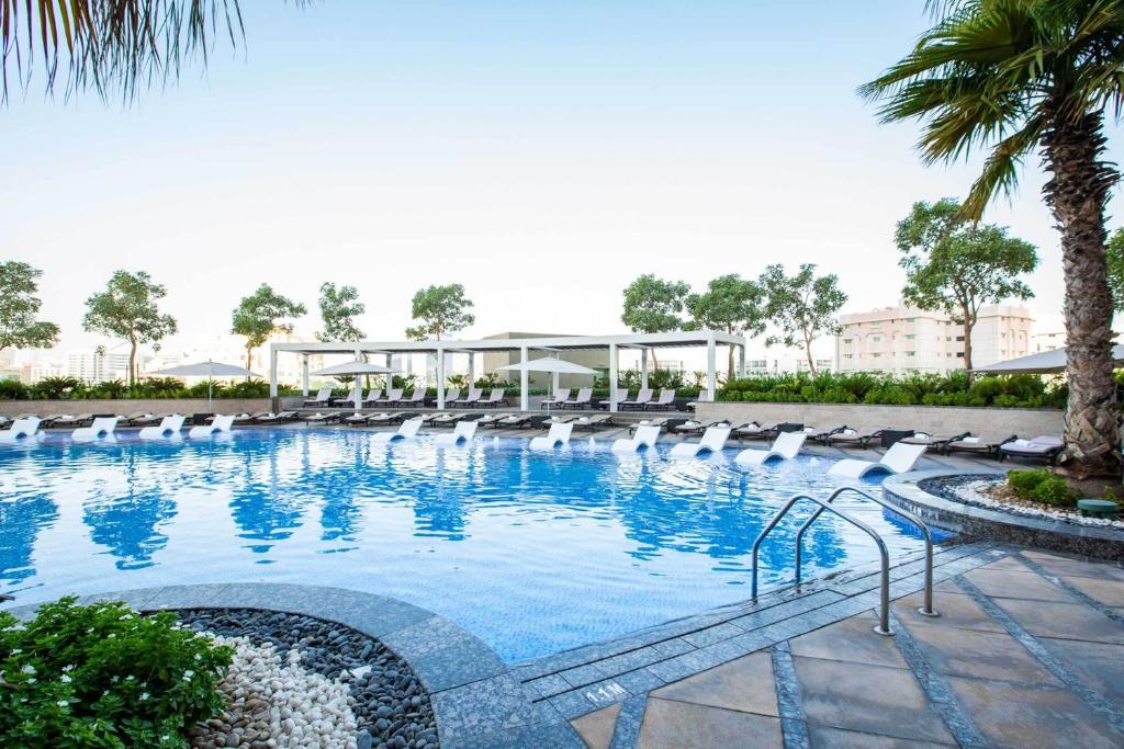 a large swimming pool with white chairs and a building at HomesGetaway-Lavish STU in Hyatt Regency Creek Heights Residences in Dubai