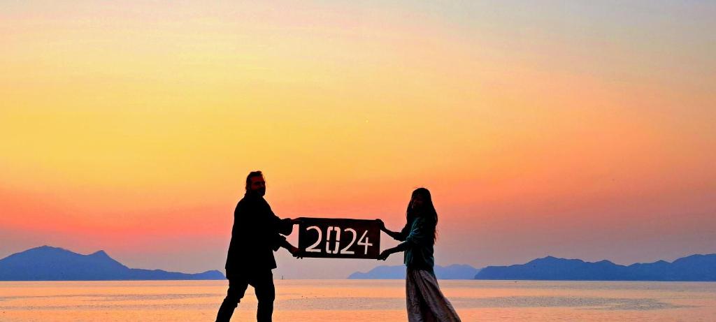 Un uomo e una donna sulla spiaggia con un cartello di イマジンウエストオーシャン（ImagineWestOcean） a Suo Oshima