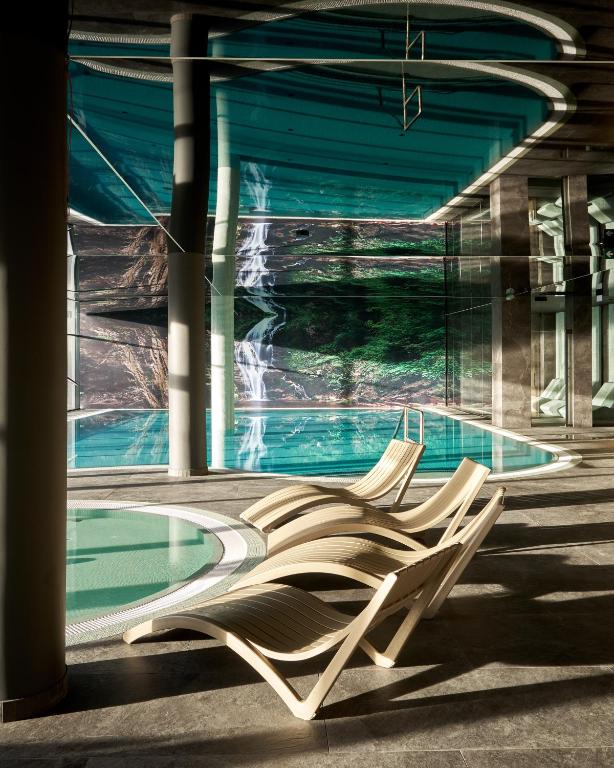 Indoor spa pool with curved loungers facing large waterfall mural, tranquil reflected light
