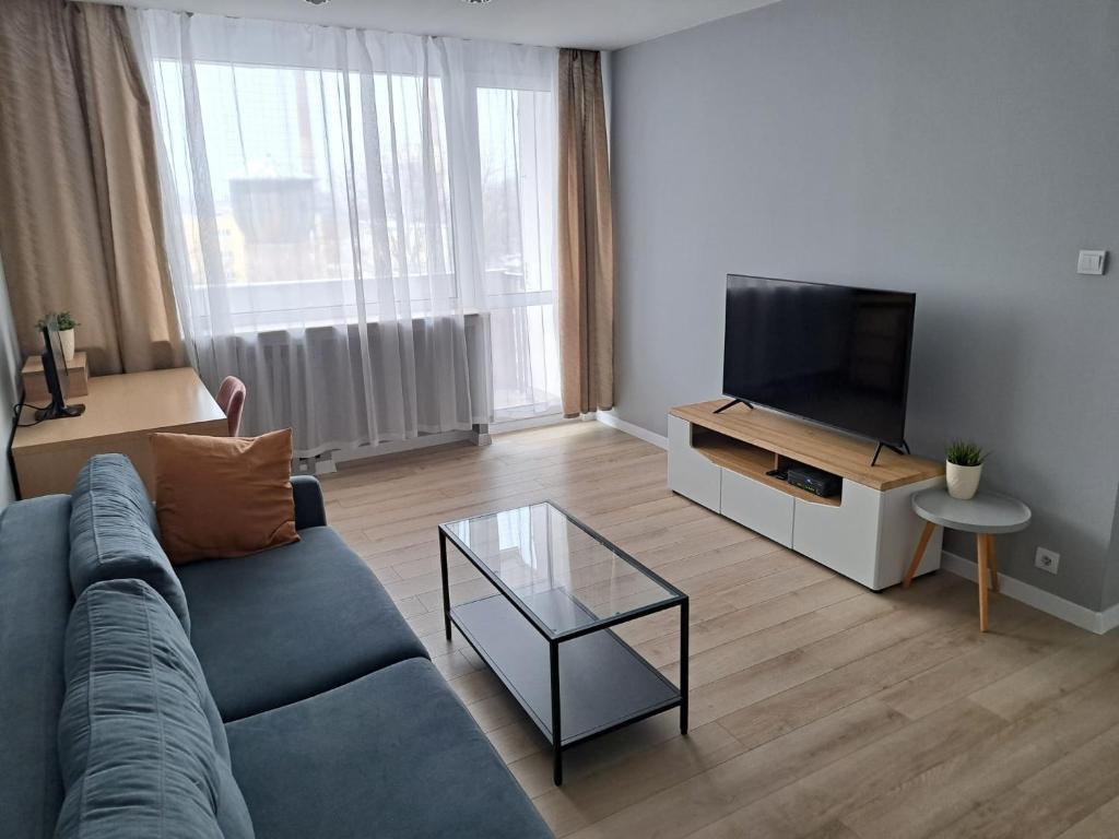 uma sala de estar com um sofá azul e uma televisão de ecrã plano em Gallusa Apartament em Katowice