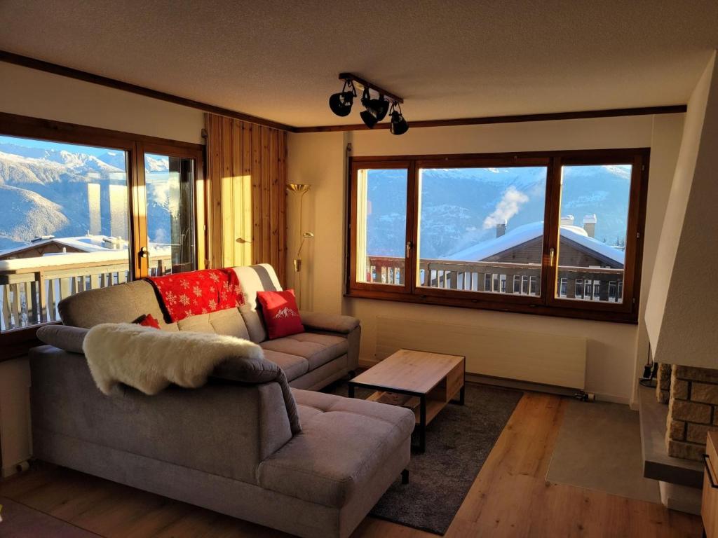 ein Wohnzimmer mit einem Sofa, einem Tisch und Fenstern in der Unterkunft Apartment Mandarin-5 by Interhome in Crans-Montana