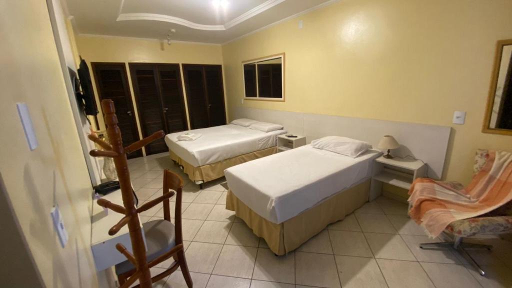 a hotel room with two beds and a chair at Pousada Emaús in Cruzeiro