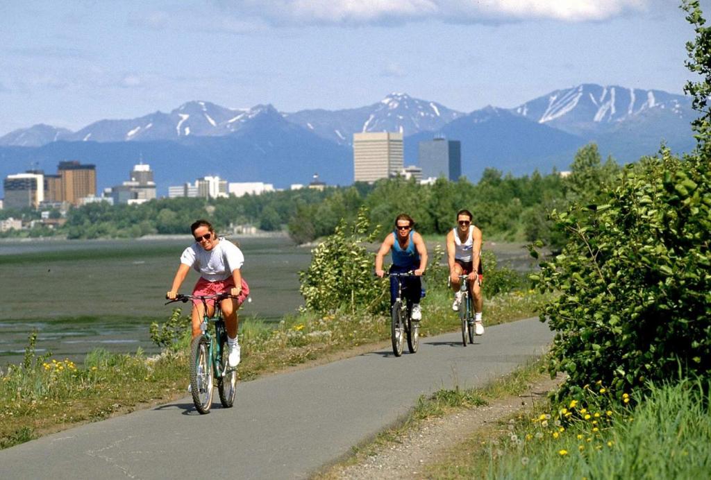 drie mensen fietsend over een weg met bergen op de achtergrond bij The Glacial Cottage Slumber Village 9 in Anchorage