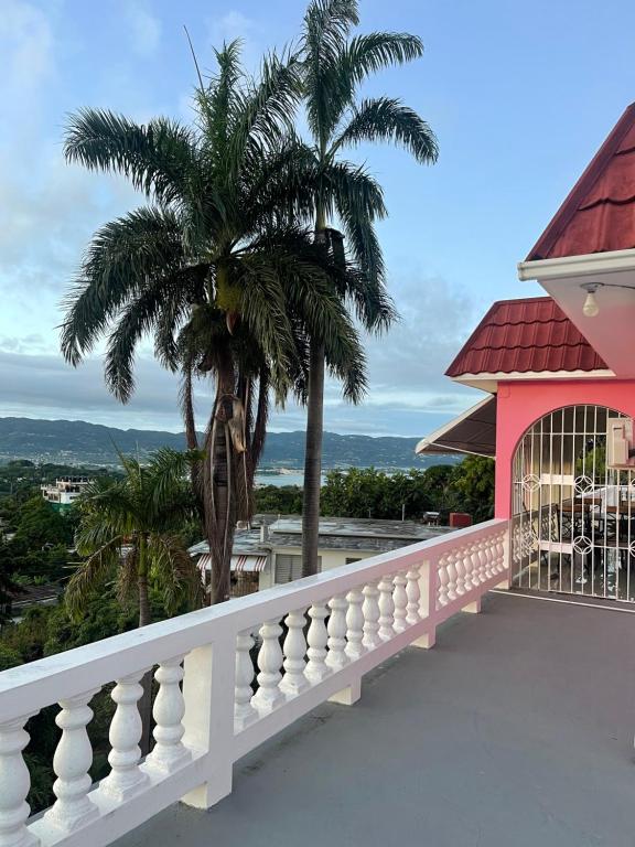 a balcony with a palm tree and a pink house at Three Palm Villa in Montego Bay