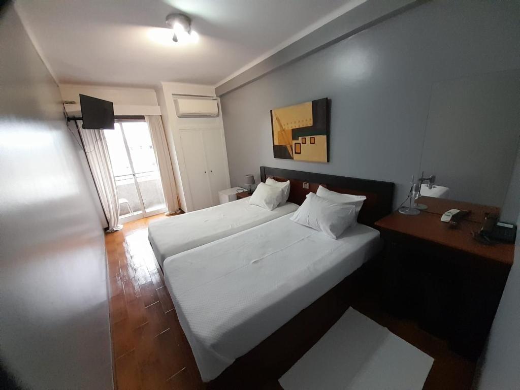 a bedroom with a large white bed and a desk at Hotel Dom Joao IV in Guimarães
