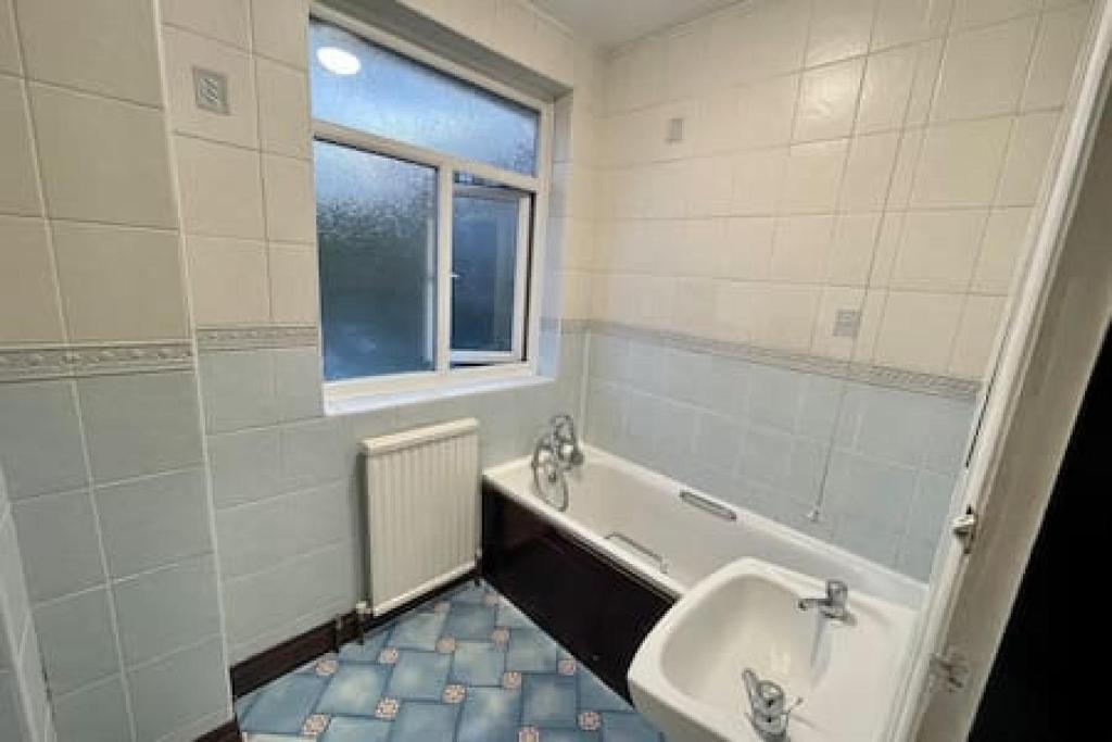 uma casa de banho com um lavatório, uma banheira e uma janela em Pair Paradise Haven - Double room em Londres