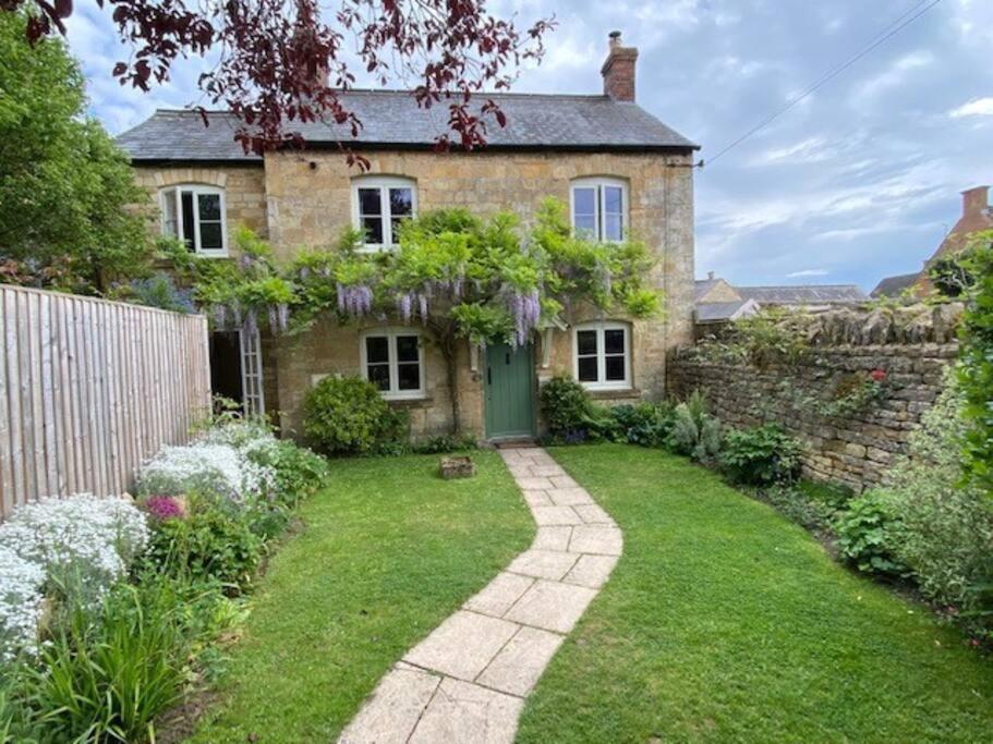 een oud bakstenen huis met een groene deur in een tuin bij The Bolt Hole, Cotswold Cottage, Moreton-In-Marsh in Moreton in Marsh