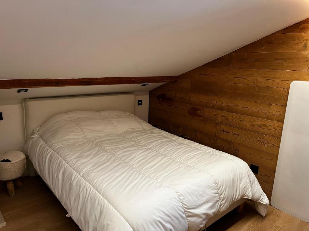 ein weißes Bett in einem Zimmer mit einer Holzwand in der Unterkunft Le Chappart in Les Carroz d'Araches