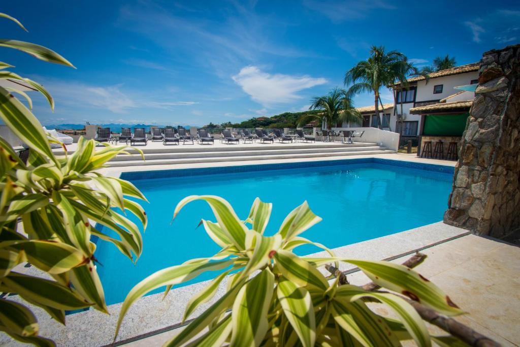 una piscina con sillas y palmeras junto a un edificio en Pousada Gammel Dansk by Latitud Hoteles, en Búzios