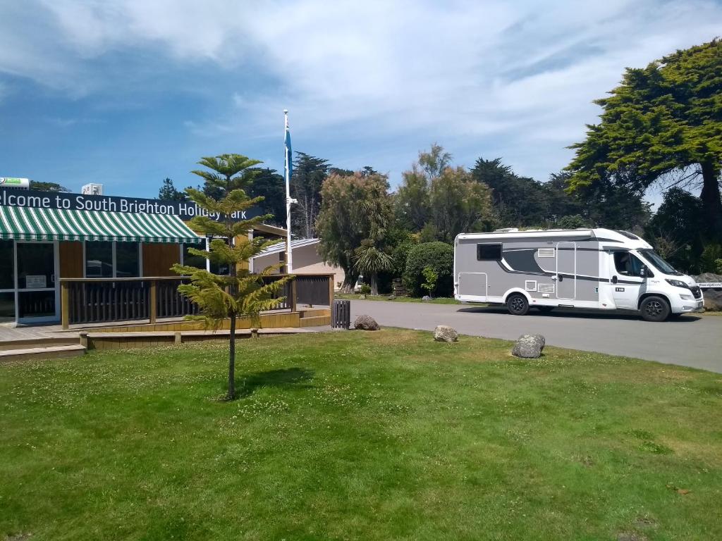 een witte camper geparkeerd voor een gebouw bij South Brighton Holiday Park in Christchurch