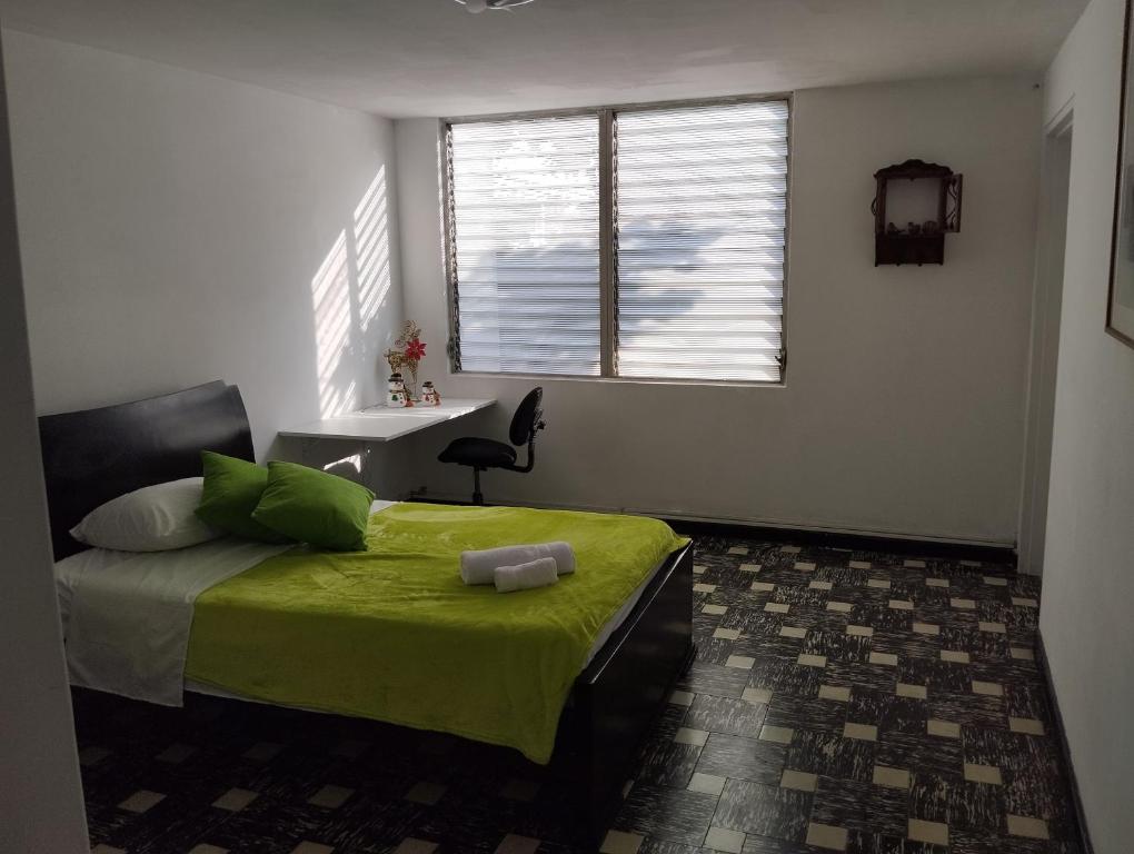 een slaapkamer met een groen bed, een bureau en een raam bij AYARANA SAN FERNANDO Habitación Cali in Cali