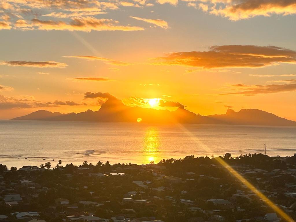 a sunset over the ocean and a city at La vue de rêve in Punaauia
