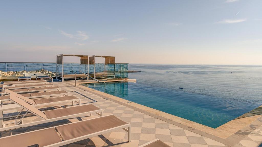 a pool with chairs and the ocean in the background at AX ODYCY Hotel in St Paul's Bay