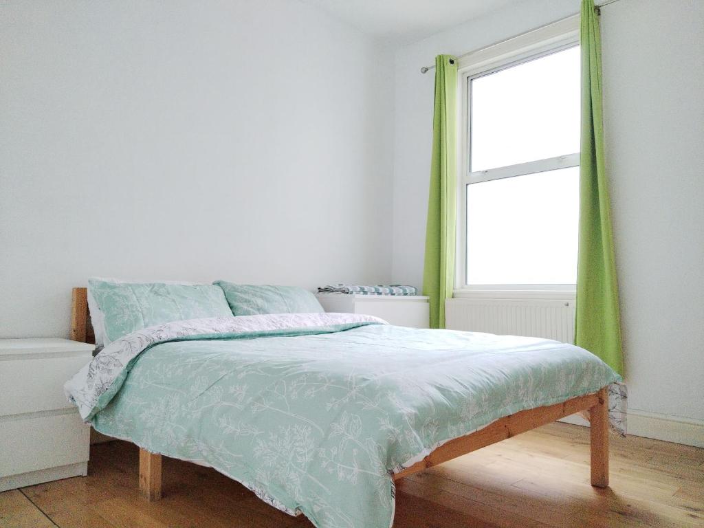 Schlafzimmer mit einem Bett mit grünen Vorhängen und einem Fenster in der Unterkunft Cosy Rooms near Canary Wharf & the O2 in London