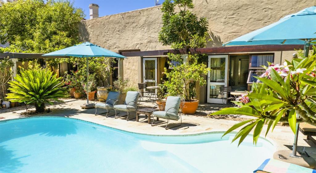 a swimming pool with chairs and umbrellas next to a house at Rosedene Lodge - 24h solar with pool and garden in Cape Town