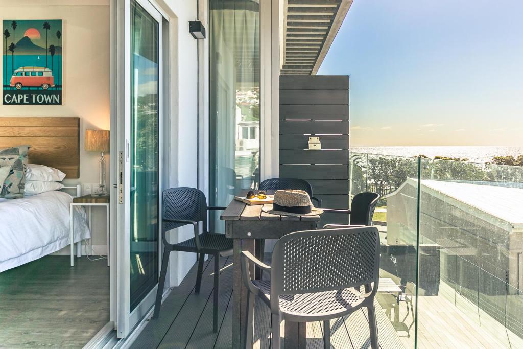 1 dormitorio con balcón con mesa y sillas en Camps Bay Village, en Ciudad del Cabo