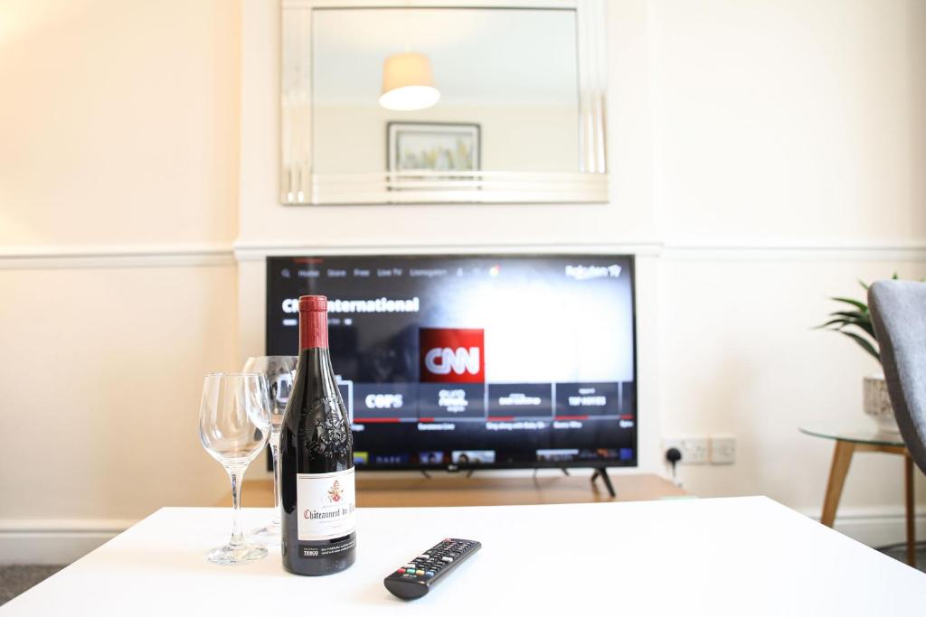 a bottle of wine and two glasses on a table with a television at Glasgow, 3 Bed Close to City Centre, Free Street Parking in Maryhill