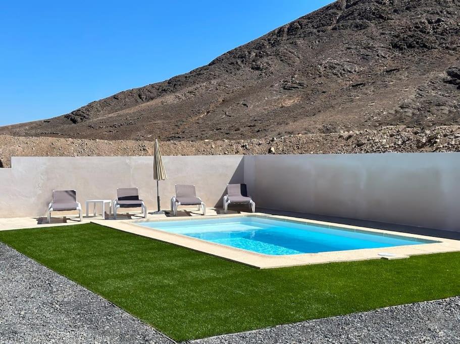 a swimming pool with two chairs and a lawn at Cómoda villa en la montaña in Gran Tarajal