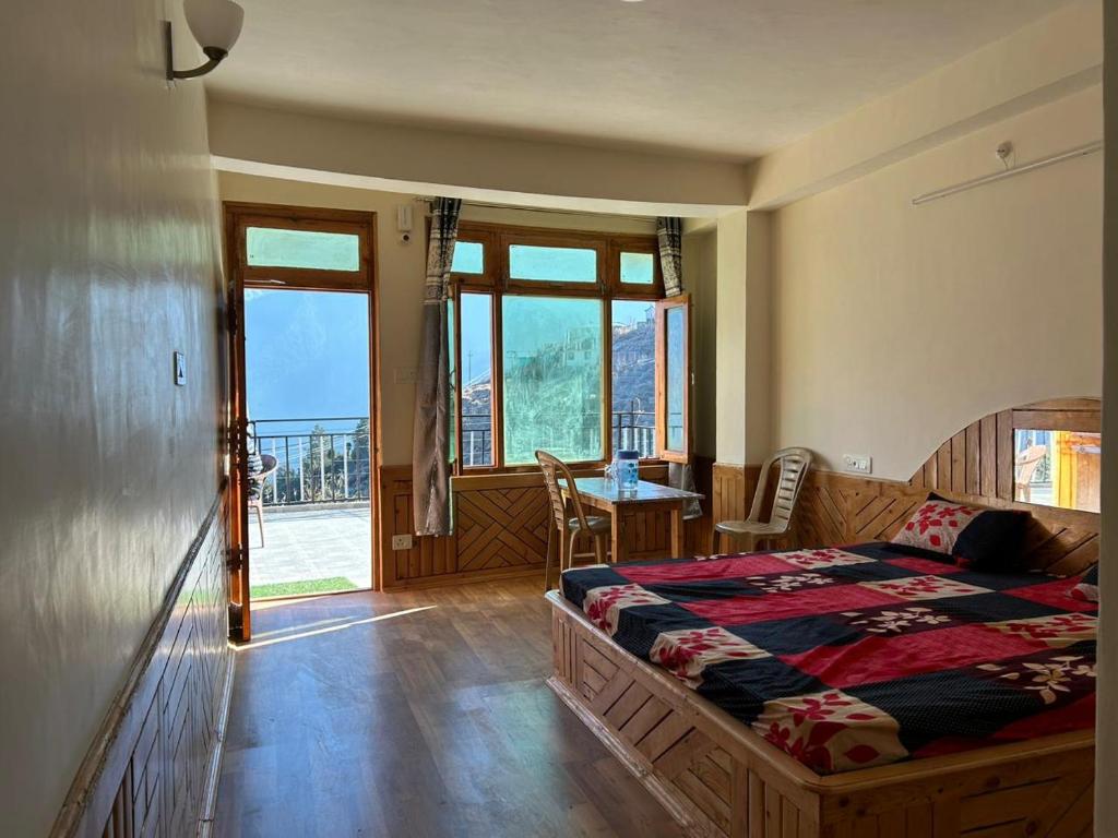 a bedroom with a bed and a table and windows at Aarav Homestay in Kalpa