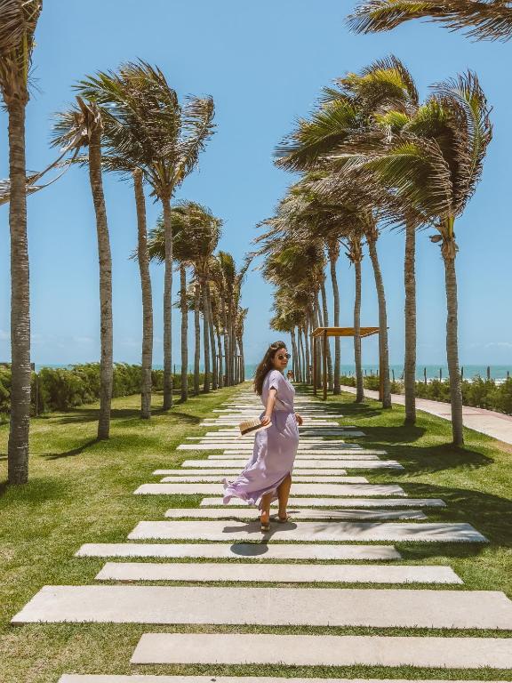 a woman standing on a stone path with palm trees at Golf Ville Resort Brisa do Golf -Apartamentos e Cobertura in Aquiraz
