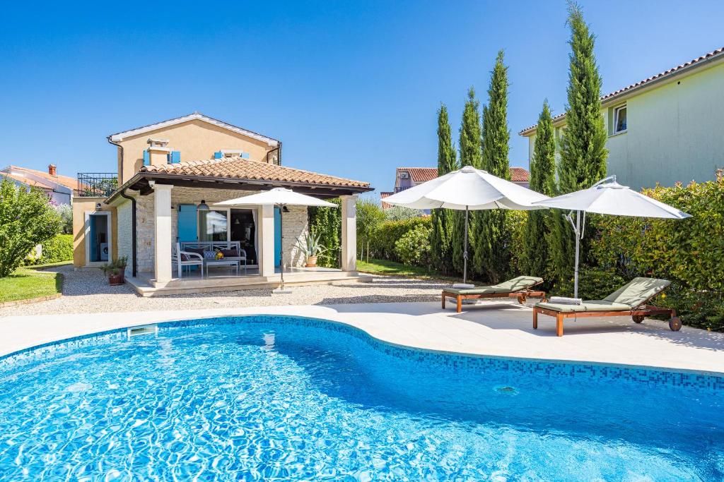 une piscine avec deux parasols et une maison dans l'établissement Villa Luka in Fažana with pool & playground only 600 meter from the beach, à Fažana