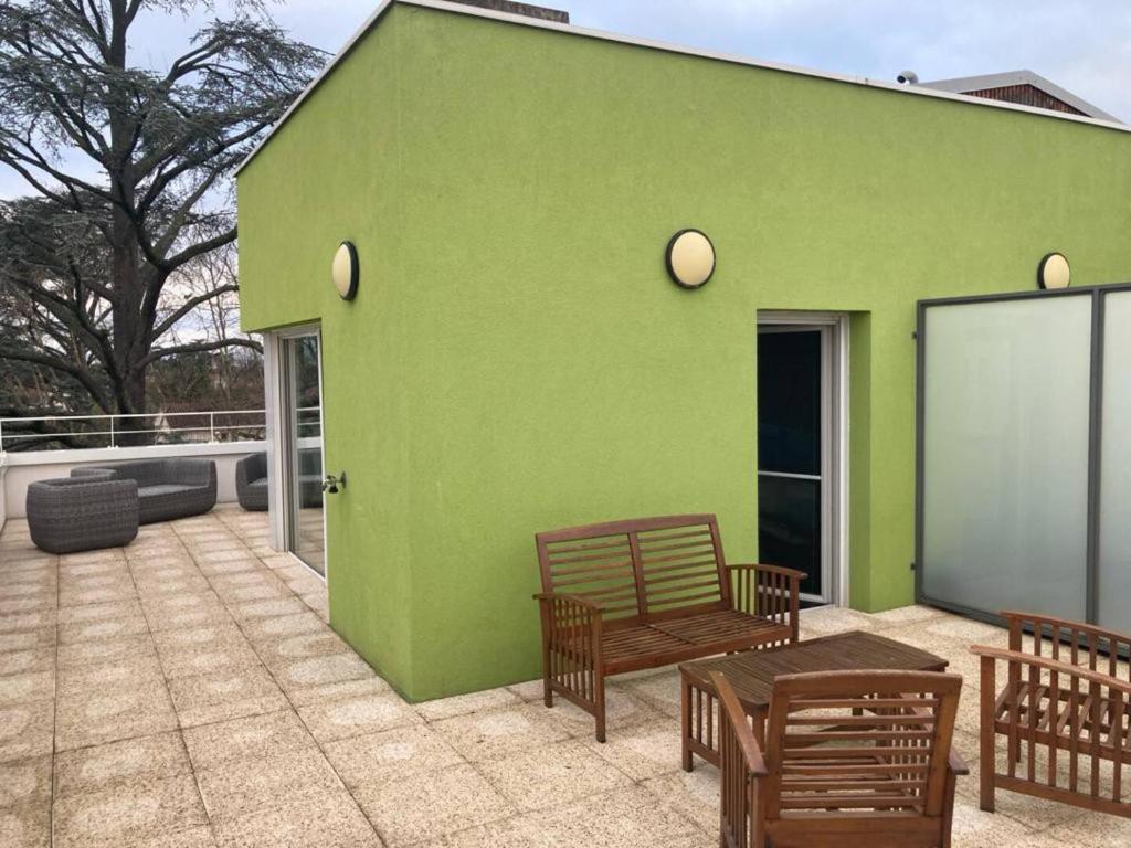 un bâtiment vert avec des bancs et une table sur une terrasse dans l'établissement Standing 3 Chambres, parkings, Terrasse, à Meyzieu