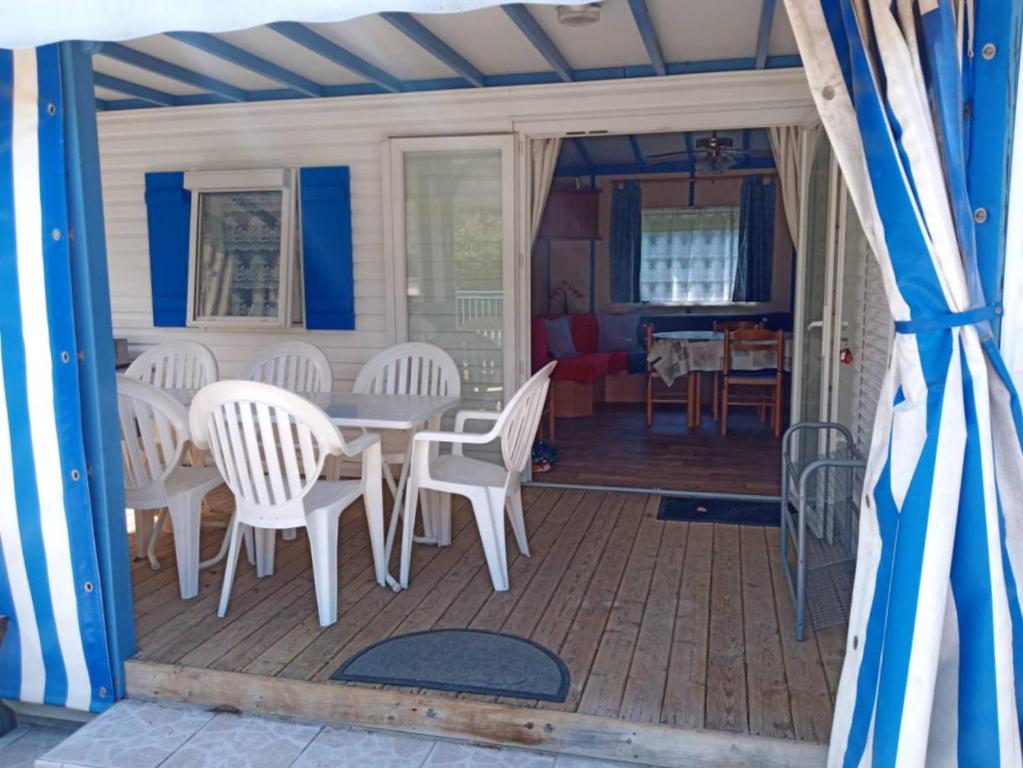 une terrasse couverte avec des chaises blanches et une table sur la terrasse. dans l'établissement La Tremblade - DECOUVREZ ce MOBIL-HOME sur un TERRAIN PRIVE, à La Tremblade