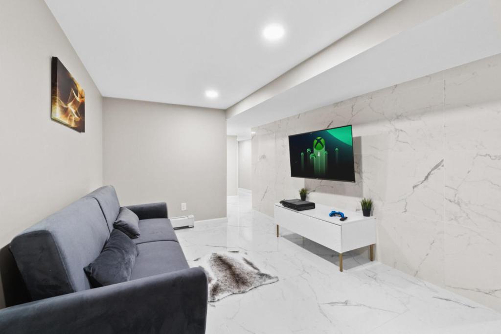 LUX White Marble Retreat near NYC في بايون: غرفة معيشة مع أريكة وتلفزيون على الحائط