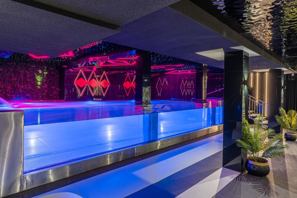 Indoor illuminated lap pool with blue glass edge, neon pink reflections and potted plants.