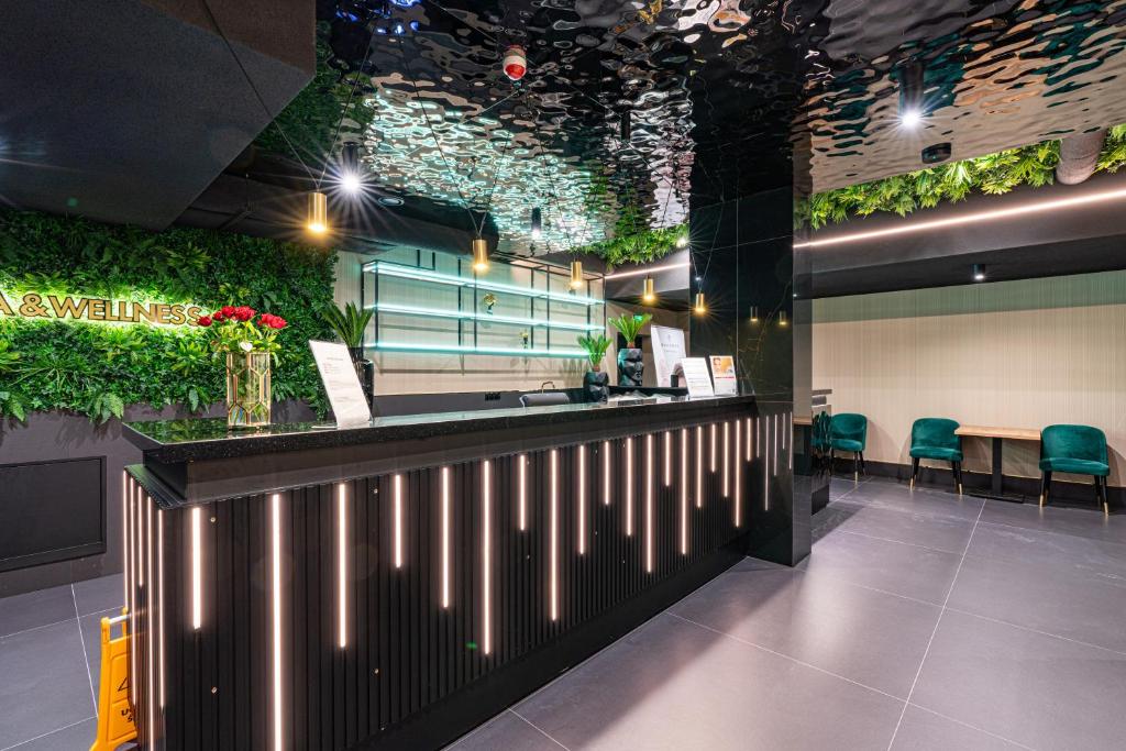 Stylish spa reception with illuminated black desk, green living wall and glossy reflective ceiling.