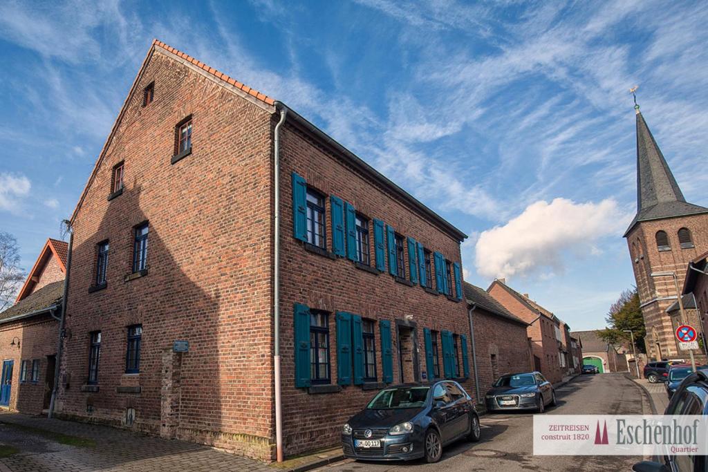 un edificio de ladrillo con ventanas azules y una iglesia en Eschenhof Quartier, en Bergheim