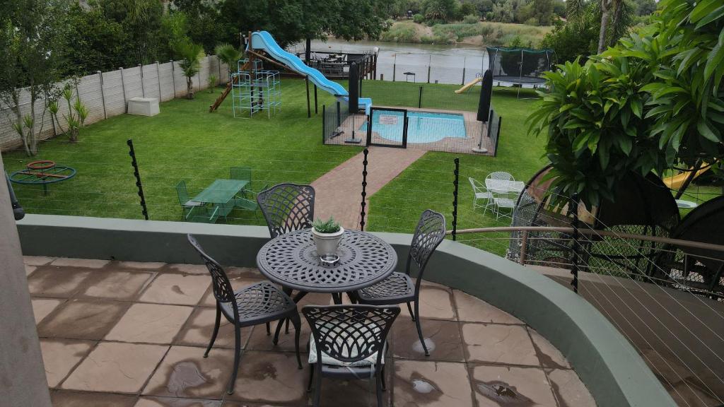 een patio met een tafel en stoelen en een speeltuin bij Moonriver Guesthouse in Upington