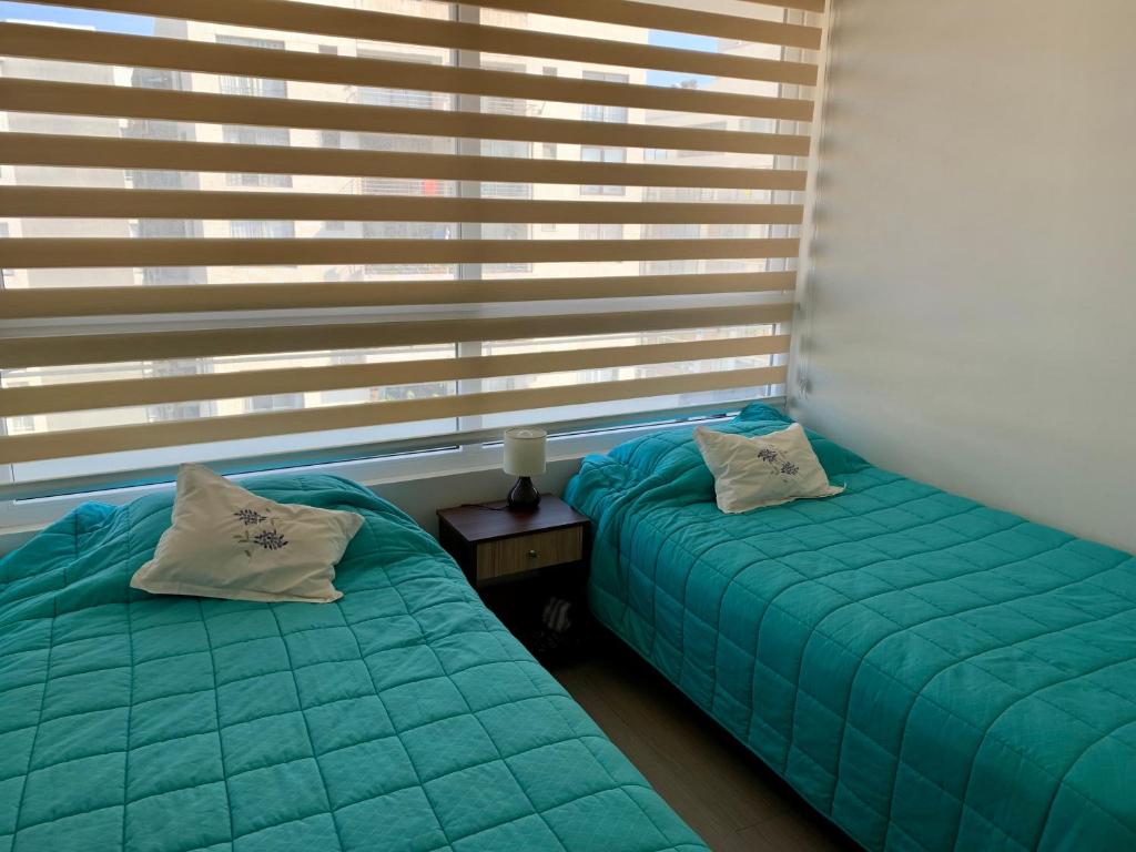 two beds in a room with windows with green sheets at Departamento nuevo, vista al Mar, Reloj de Flores in Viña del Mar