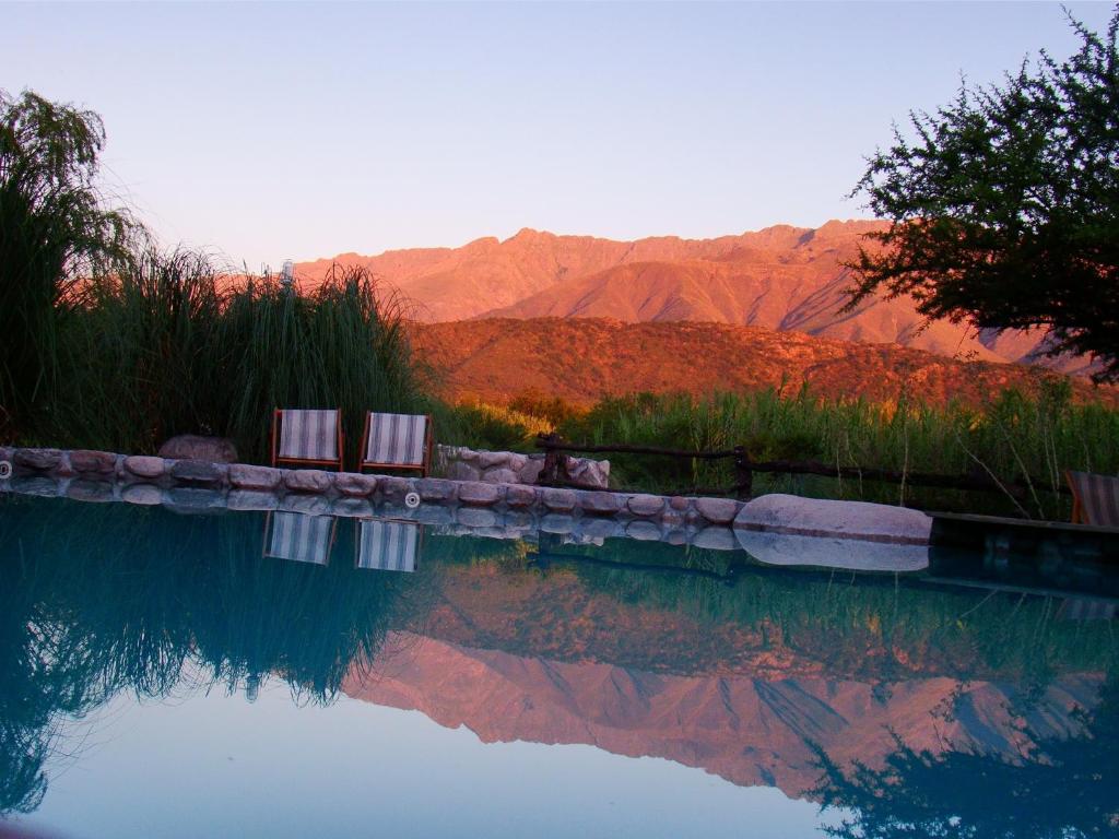 una piscina de agua con dos sillas y montañas en el fondo en Posada La Valentina en Villa Las Rosas