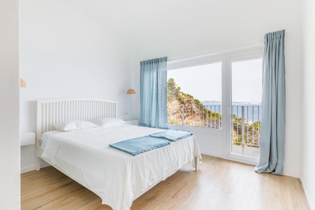 Dormitorio blanco con cama y ventana grande en Cap Sa Sal Aquamarina Begur, en Begur