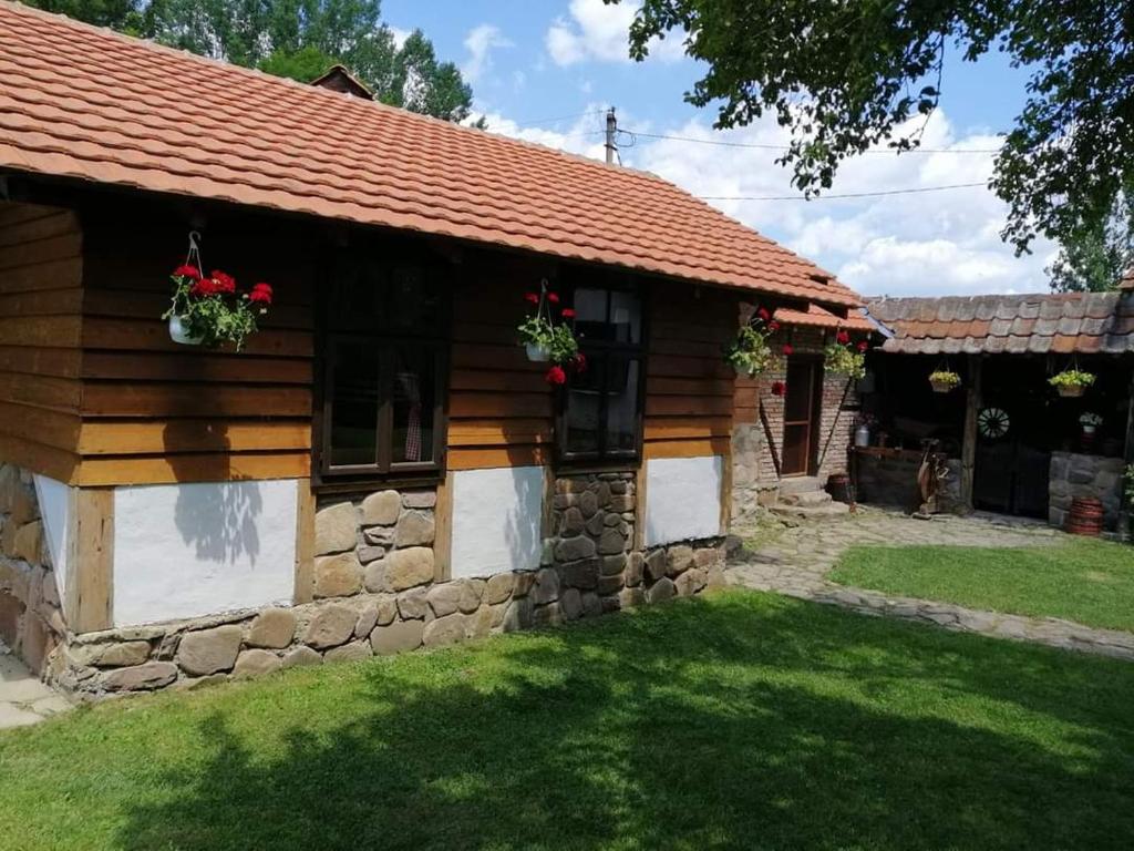 a log cabin with a stone wall and flowers on the windows at Etno kuca Nikolov in Dimitrovgrad