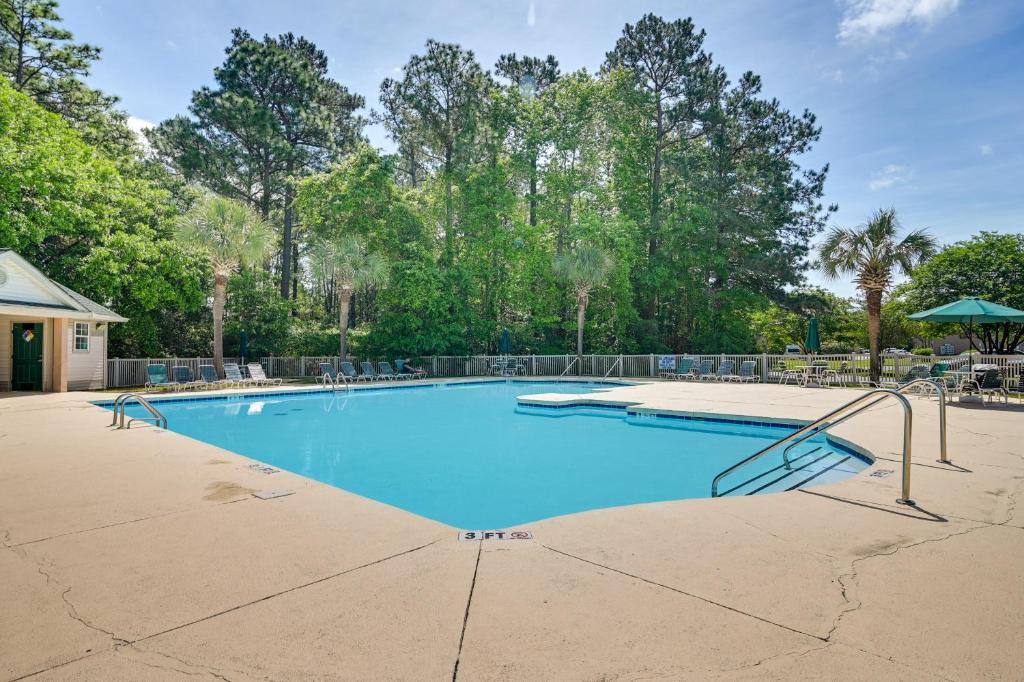 a large swimming pool with blue water and trees at Pawleys Island Condo with Screened Porch and Golfing! in Pawleys Island