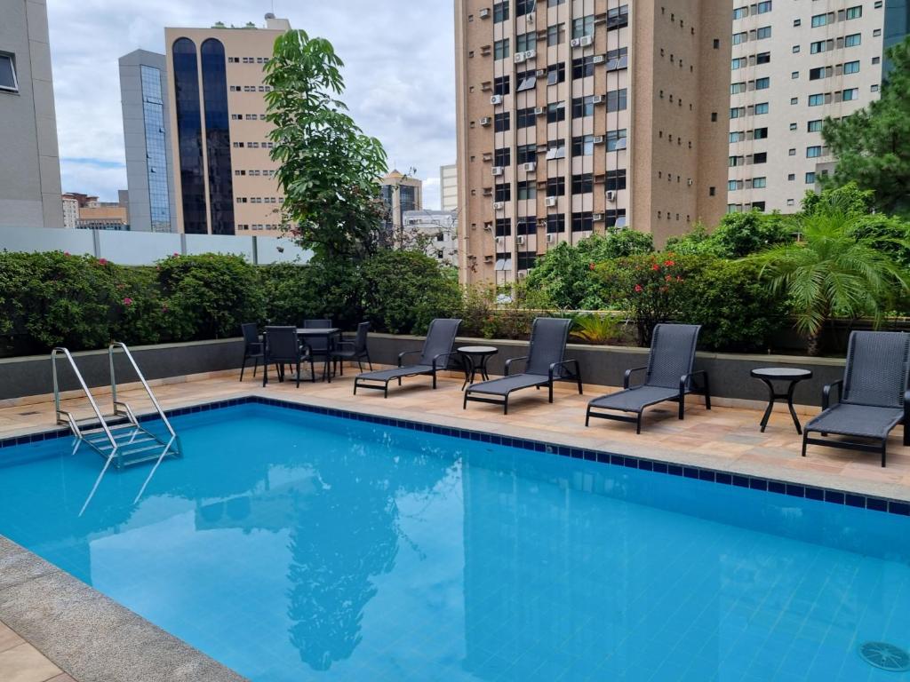 uma piscina com cadeiras e mesas num edifício em Condomínio Max Savassi Superior apto 1502 em Belo Horizonte