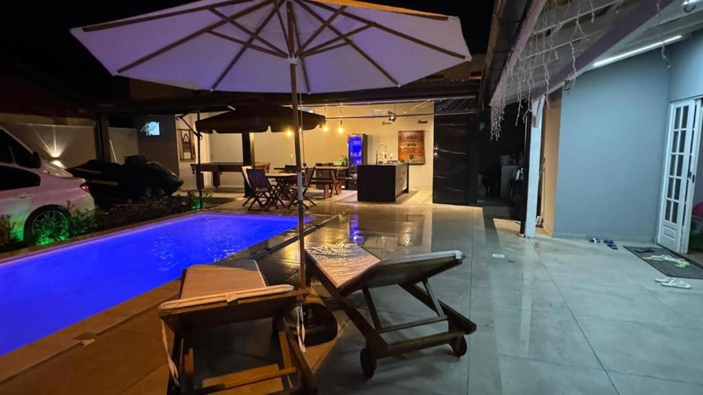 una piscina con ombrellone e sedie viola e tavolo e piscina di CASA DE PRAIA -Palmas Governador Celso Ramos, Sc a Governador Celso Ramos