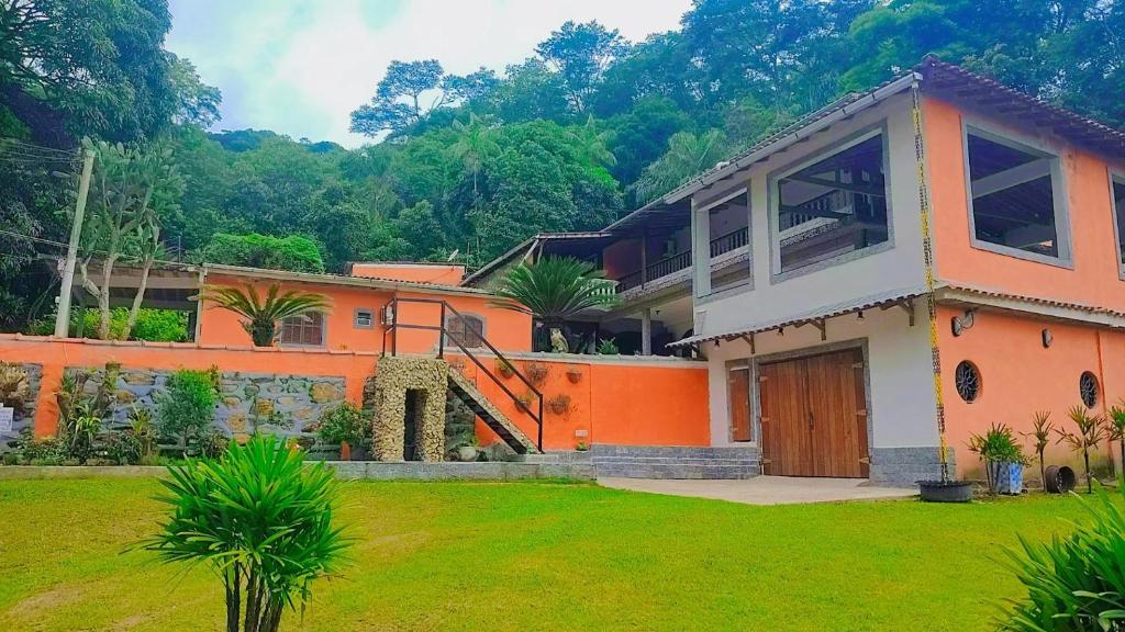 una casa arancione con un cortile verde e alberi di Casa tia Rosa hospedagem familiar a Guapimirim