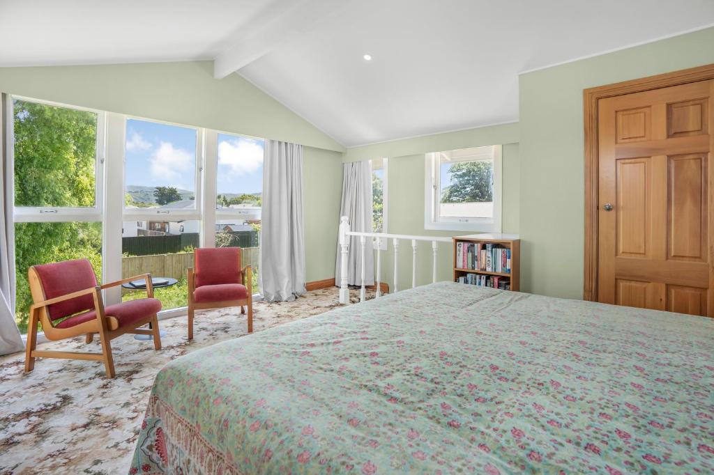 a bedroom with a bed and two chairs and windows at Farley Avenue Turret & Lounge in Greytown