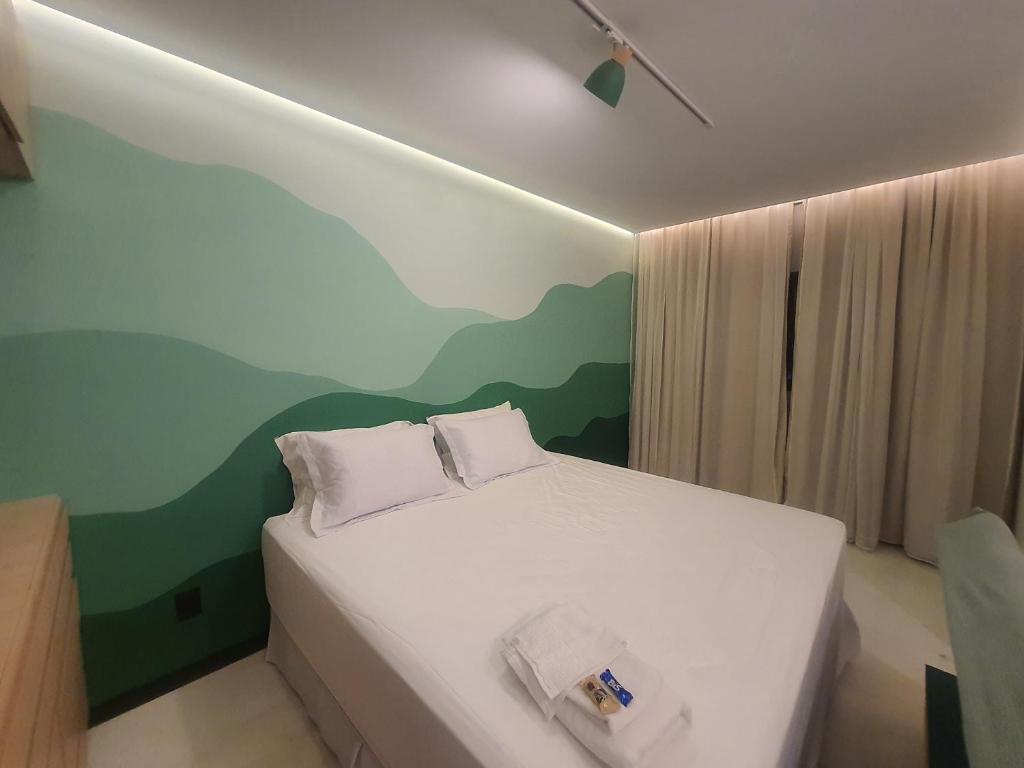 a bedroom with a white bed with a painting on the wall at Theotokos Flats Apart-hotel in Piumhi